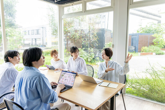 緑が見える明るいオフィスで会議をする5人の日本人ビジネスチーム