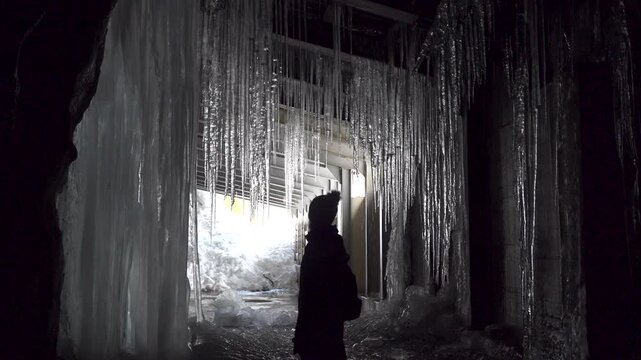 Silhouette of female traveller exploring mysterious tunnel with hanging icicles