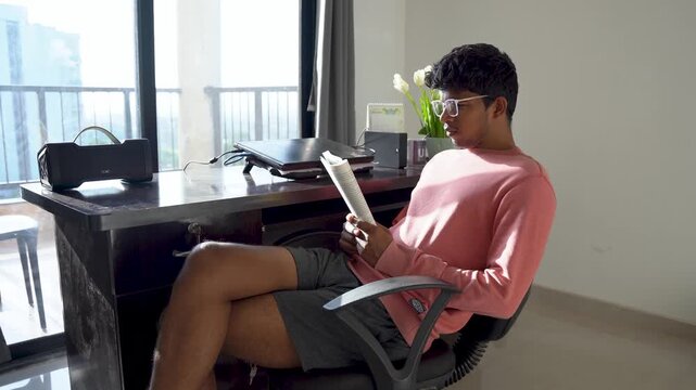 Young man deeply engaged in reading while relaxing in an office chair inside a modern home workspace.