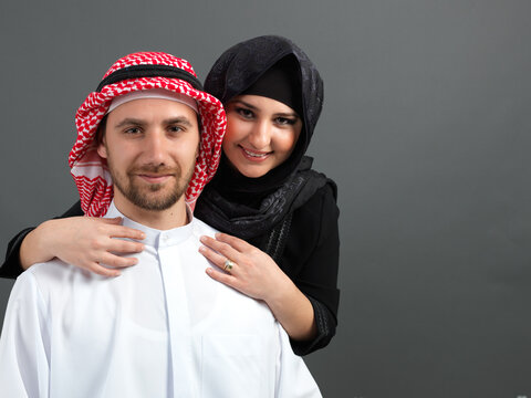 Close up portrait of happy smiling Arab couple in traditional clothing embracing isolated on grey background.