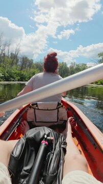 First-person POV of mature couple paddling tandem kayak on calm river for summer recreation