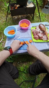 Man slicing fresh carrot with knife on folding table for outdoor picnic barbecue camping lifestyle