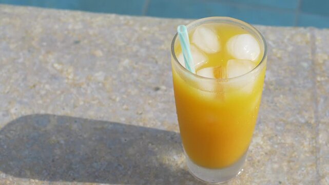 Close up of orange juice with ice cubes and drinking straw in transparent glass. Golden citrus beverage appears cool and inviting, presenting refreshing drink details for food service menus