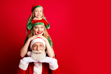 Naklejka premium Santa Claus with two cheerful family elves — mother and daughter in Christmas outfits smiling against a red background