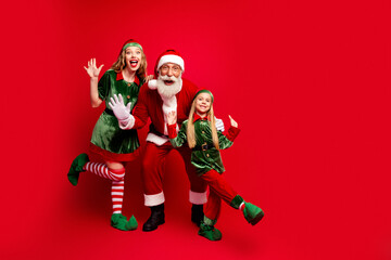 Naklejka premium Santa Claus with two cheerful elves posing and waving against a red background, festive family holiday portrait capturing joy, celebration and seasonal Christmas fun