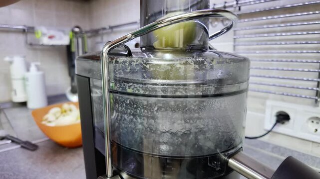 Electric juicer crushing fresh green apple pieces in kitchen for healthy lifestyle