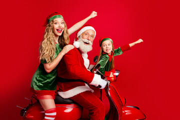Naklejka premium Santa rides a red scooter with two cheerful elves celebrating Christmas joy and playful holiday spirit on a vibrant red background