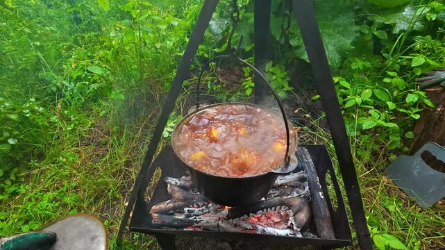 Man opening cauldron lid with boiling stew over campfire for outdoor camping cooking lifestyle