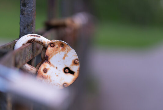 A white heart-shaped padlock attached to a metal bridge railing in Latvia. The lock shows visible signs of rust and weathering, adding character and a sense of history to the scene. 