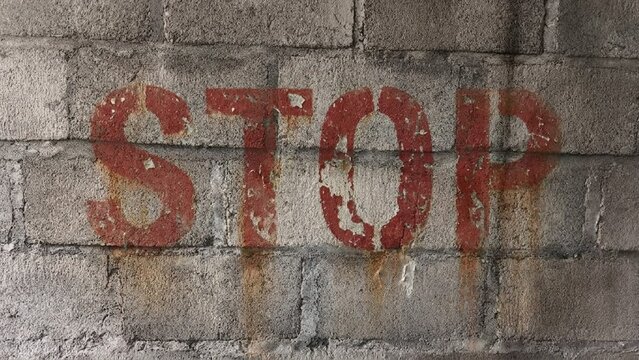 Red "STOP" word stenciled on a weathered concrete block wall
