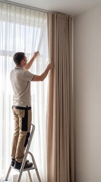 Handyman hanging fabric drapes on window track