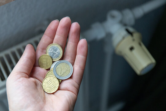 Hand holding euro coins near home heating radiator. Counting euro cents to pay for expensive winter heating bills.