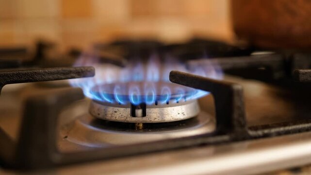 Bright blue flame burning on a modern gas stove burner in a kitchen setting.