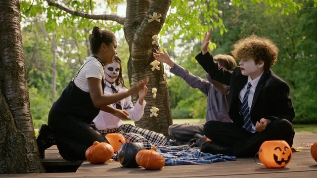 Multiethnic teenagers in Halloween costumes throwing autumn leaves and giving high fives outdoors. Ideal for autumn holiday campaigns, party promotions, and seasonal youth marketing