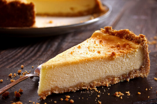 New York Cheesecake on a Rustic Wooden Background.

A slice of classic New York cheesecake with a creamy texture and graham cracker crust, served on a plate over a dark rustic wooden background. 