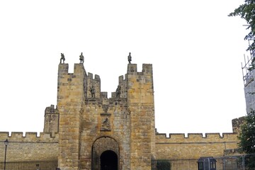 Looking up at high medieval stone castle walls and towers against white sky. Historic fortress architecture, ancient defensive structure. Alnwick castle England © TomKorcak