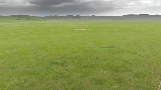 Stone kurgan and sacred stele stand on Mongolia steppe as ancient burial monument.