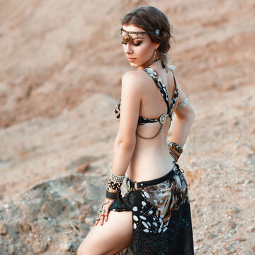 Pretty woman in an Indian tribal jewelry on a background of sand. Tribal fusion dance style.