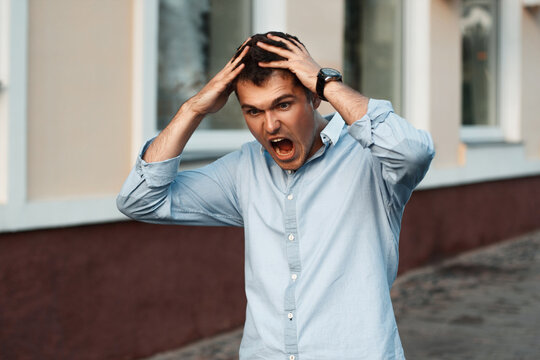 Portrait of young angry man with hands on head. Clings to his head and shouts