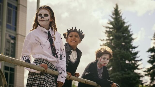 Diverse teenagers in spooky Halloween costumes leaning on railing, pointing away and running in excitement. Clip serves seasonal event marketing and autumn holiday commercials