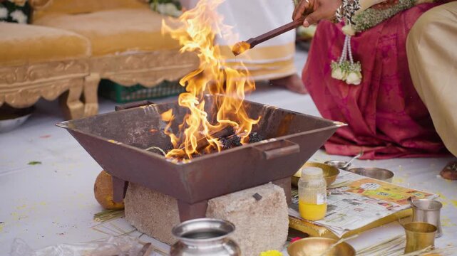 Sacred havan fire burns in a metal kund as the groom performs ritual offerings by pouring melted ghee during a South Indian Karnataka wedding.