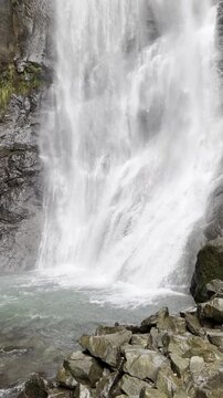 Vertical shot of a mountain waterfall flowing into a crystal clear pool.