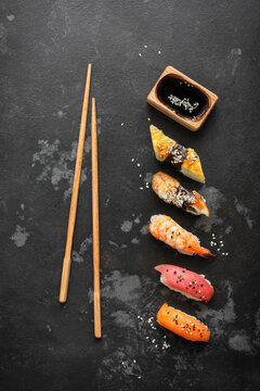 Set of Japanese sushi with soy sauce and chopsticks on a black stone background, top view, flat lay, copy space, vertical
