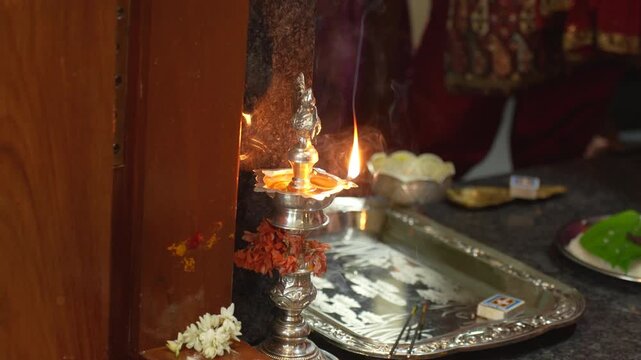 TraditionaI brass oil lamp burns at a South Indian wedding home entrance with flowers, incense and offerings in slow motion.