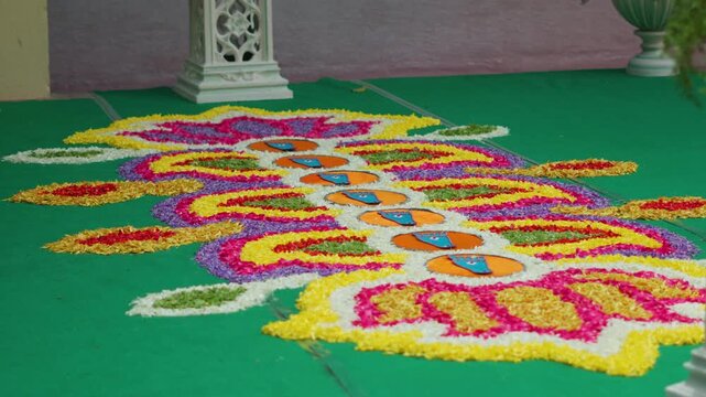 Wide view of colorful flower rangoli with blue footprint cutouts on orange circles in slow motion during a South Indian Karnataka wedding Saptapadi ritual.