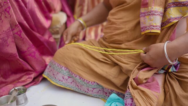Close view of a Kannada wedding ritual as a male priest in dhoti slowly twists a yellow sacred thread on the floor.