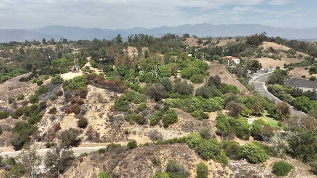 Los Angeles, California, USA - Aerial drone view over Elysian Park West Loop Trailhead featuring an expansive mountain range in the distance. The footage captures green hillsides, hiking tr