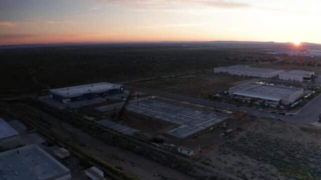 High aerial panning shot of a desert construction site with sun flare at dawn in Palmdale, California. 4K