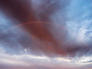 Obraz premium Faint Rainbow Beneath Dramatic Storm Clouds After Rain at Sunrise