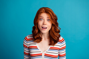 Fototapeta premium Surprised redhead woman with striped sweater looking amazed against a bright blue background