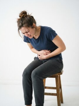 Young woman sitting on a stool suffering from severe abdominal pain or stomach ache, isolated on white background