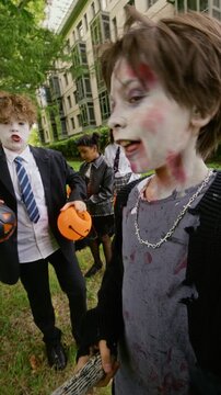 Portrait of Caucasian teenage boy with zombie makeup holding toy axe outdoors with diverse friends celebrating Halloween. Footage fits seasonal youth promotions, vertical