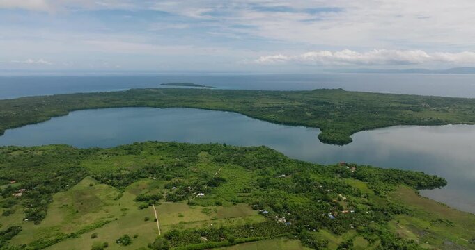 Blue lake surrounded by forest and farmland with the sea in the distance. Camotes, Philippines.