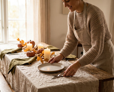 Welcoming woman arranging pumpkins and candles on rustic autumn dinner table