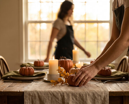 Attentive hand placing mini pumpkin beside candle on autumn dinner table