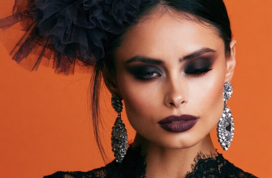 Woman wearing black makeup and ornate silver earrings against a vibrant orange