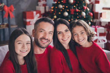 Naklejka premium Happy family wearing matching red sweaters smiling together by a decorated Christmas tree with wrapped gifts at home