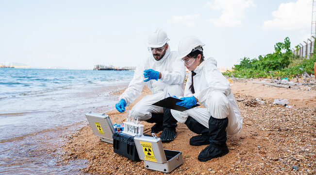 Scientists biologists and researchers in protective suits taking water samples from waste water from industrial. Experts analyze the water in a contaminated environment.