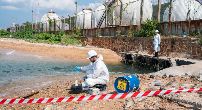 Scientists biologists and researchers in protective suits taking water samples from waste water from industrial. Experts analyze the water in a contaminated environment.