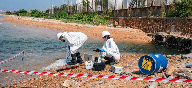 Scientists biologists and researchers in protective suits taking water samples from waste water from industrial. Experts analyze the water in a contaminated environment.