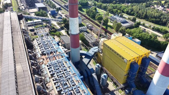 Aerial view of an industrial plant showcasing a series of large pipes and machinery, with blue roofs and structural elements visible, highlighting the complexity of the factory layout and design