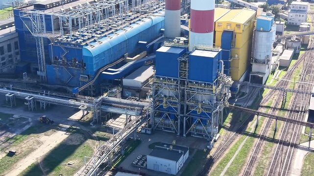Industrial power plant with blue and yellow structures, featuring smoke stacks and extensive piping, captured from an aerial perspective showcasing the facility's layout and operational elements