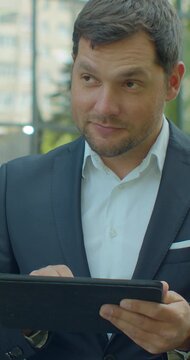 Vertical video. Man Holding Modern digital tablet. Businessman Typing on his digital tablet. businessman read news on Tablet Computer. Classical Black Suit. Business Lifestyle.