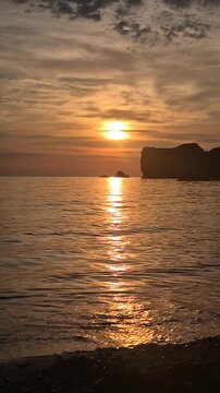 Golden sunset ocean landscape with calm waves rolling over the rocky beach shore. Static long shot.