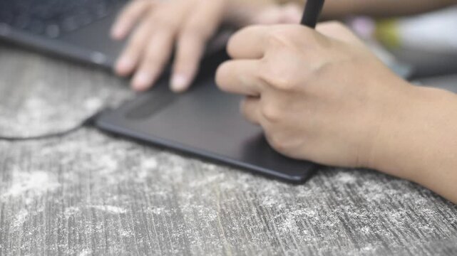 Close up shot of an artist or illustrator hand using a stylus pen drawing on a digital graphic tablet, working on a laptop at a wooden desk. Concept for digital art creation, graphic design, remote