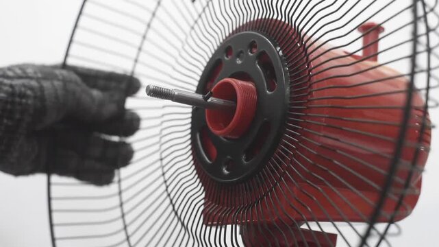 Close-up shot of a technician wearing protective work gloves assembling and locking the back grille onto an electric fan motor unit on a white background. DIY home appliance repair and maintenance con